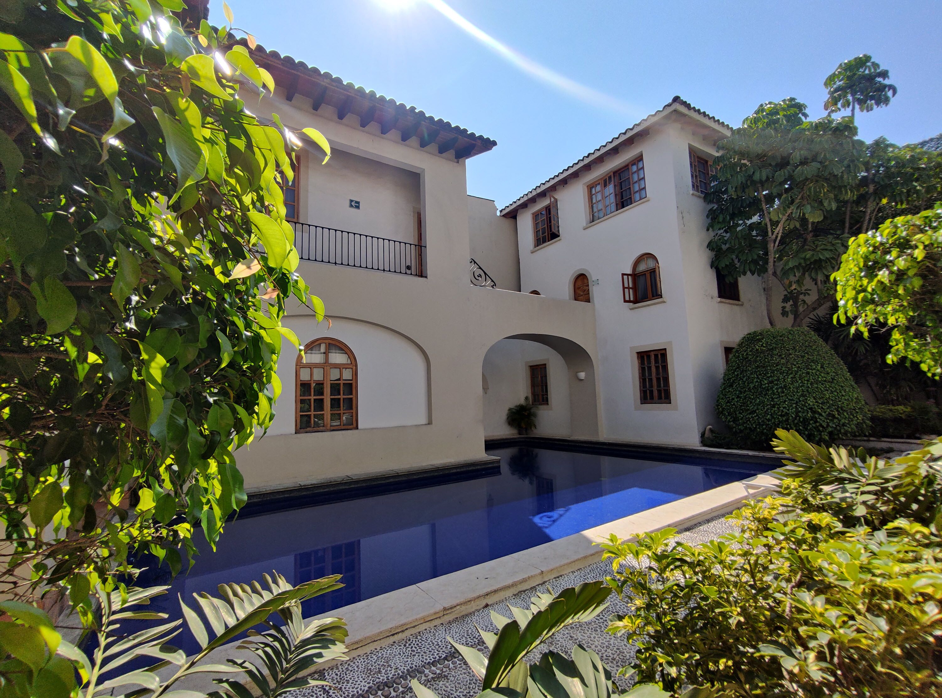 A two-story building with a swimming pool, surrounded by lush greenery.