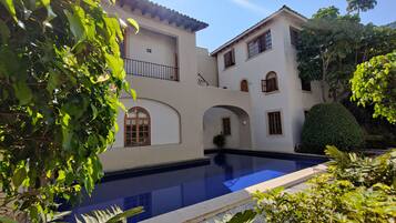 A two-story building with a swimming pool, surrounded by lush greenery.