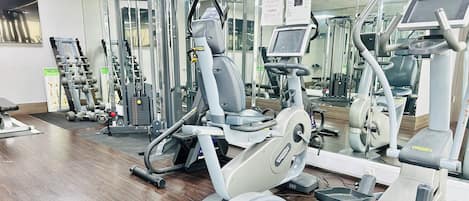 Un gimnasio con diversas máquinas de ejercicio, entre ellas cintas de correr, elípticas y máquinas de pesas.