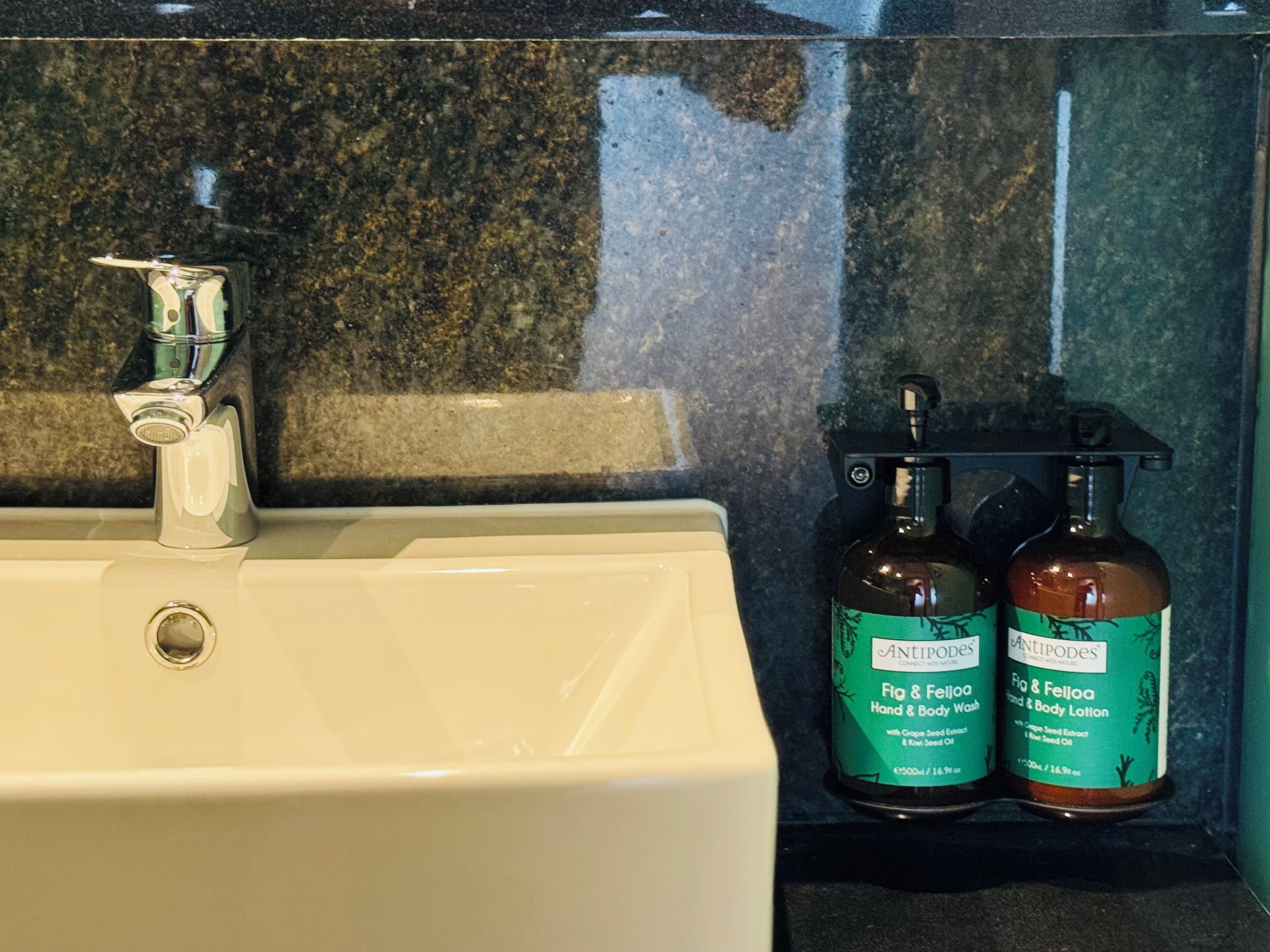 A bathroom sink with a chrome faucet and two bottles of Antipodes body wash and lotion on the countertop.