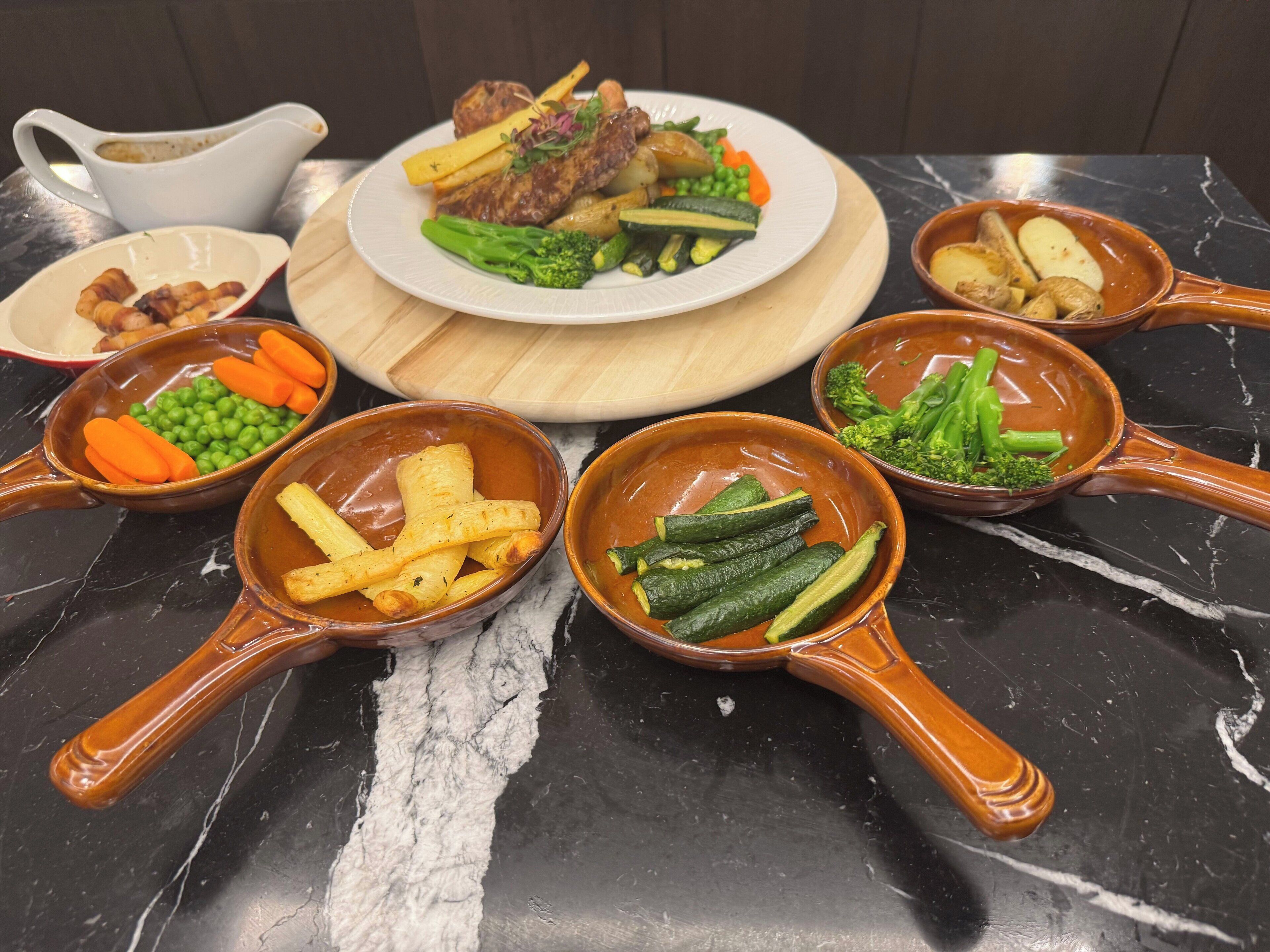 Una mesa con diversos platos, incluyendo carne, verduras y una salsera.