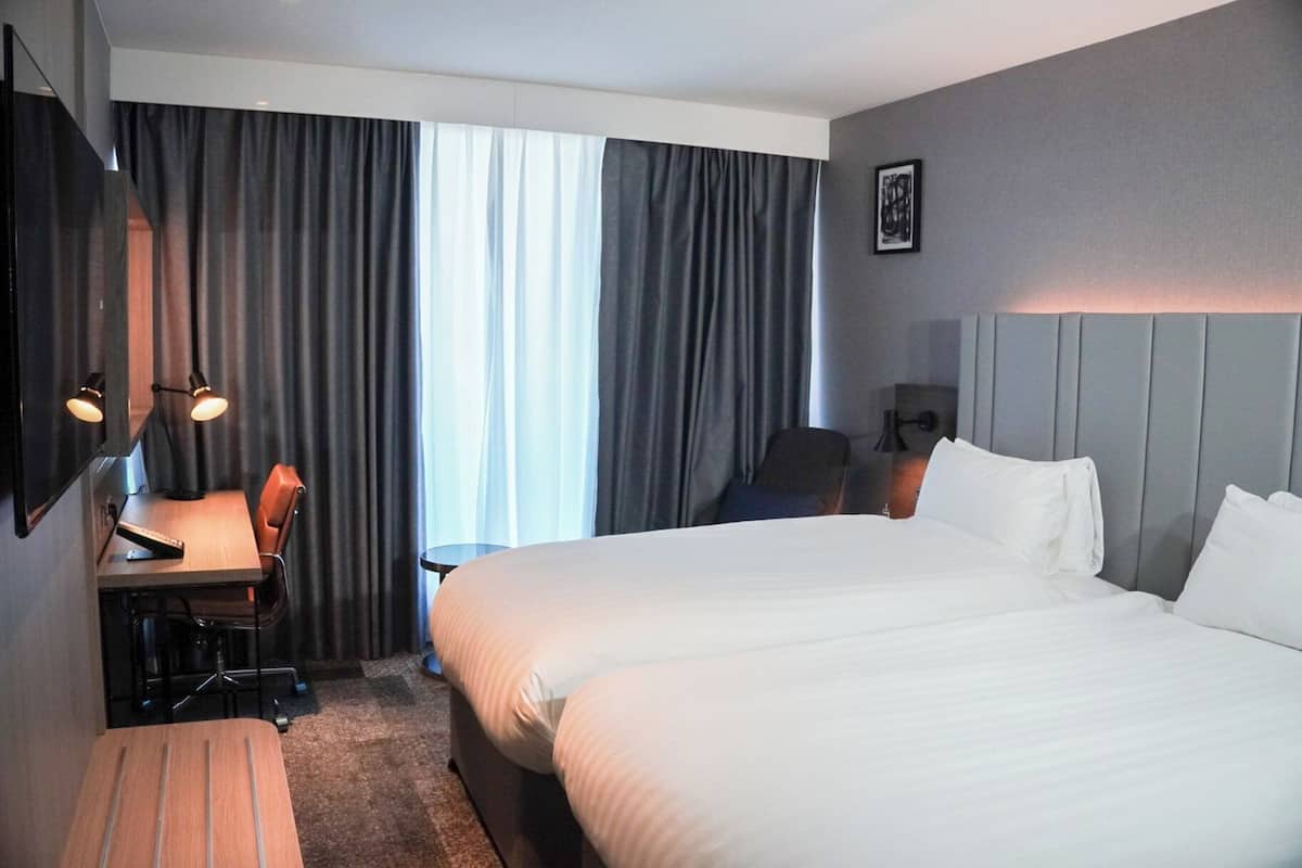 Een hotelkamer met een groot bed, een bureau met stoel, een televisie en een raam met gordijnen.