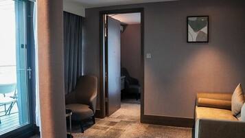 Habitación de hotel con un ventanal grande, una silla, un sofá y una puerta que da a otra habitación.