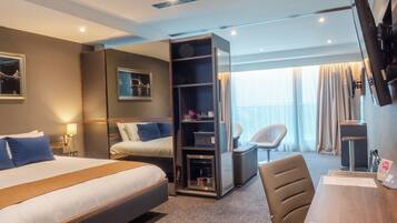 A hotel room with a bed, a desk with a chair, a TV, and a minibar.