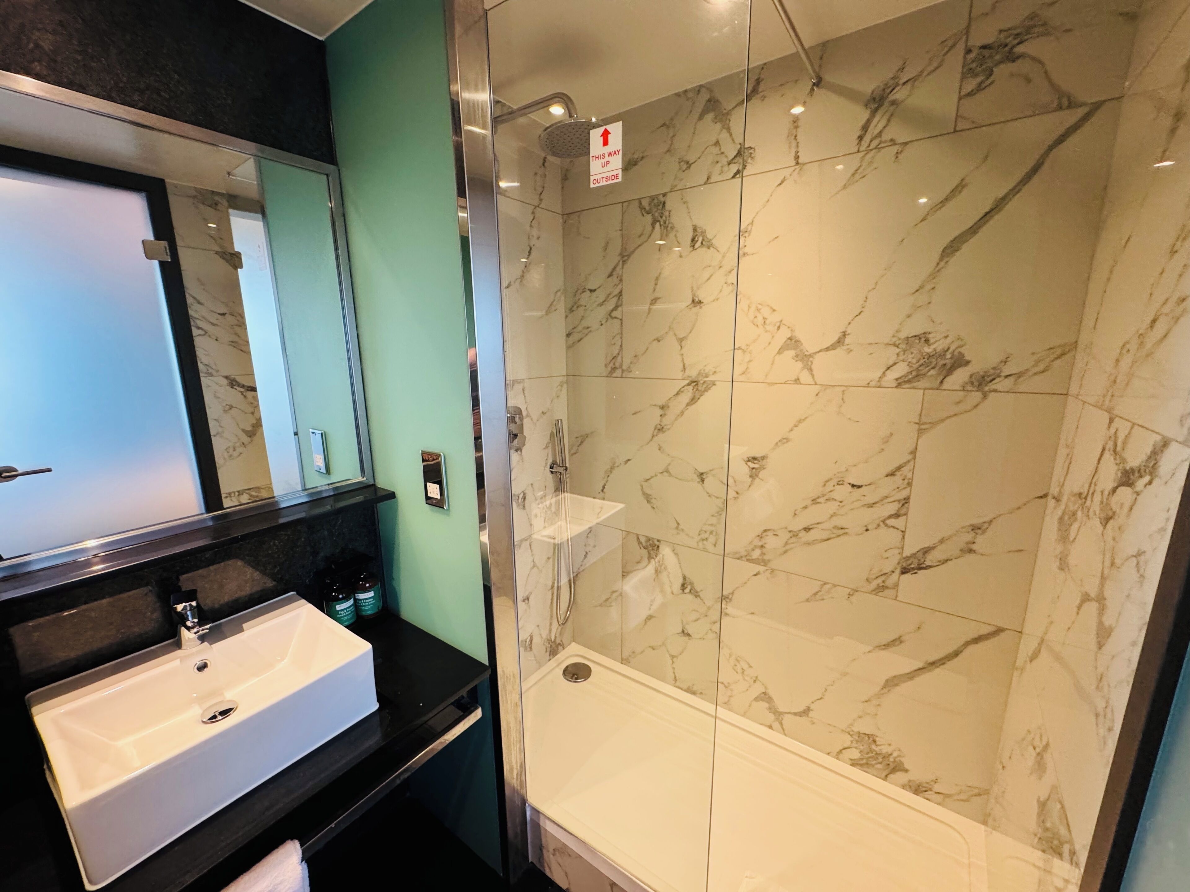 Une salle de bain moderne avec une douche en marbre, un lavabo et un miroir.