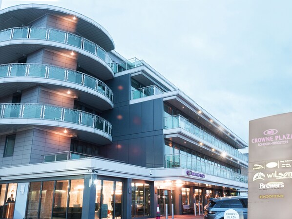 Een meerlaags gebouw met een glazen gevel, meerdere balkons en een gelijkvloerse ingang met signage voor Crowne Plaza London-Kingston.