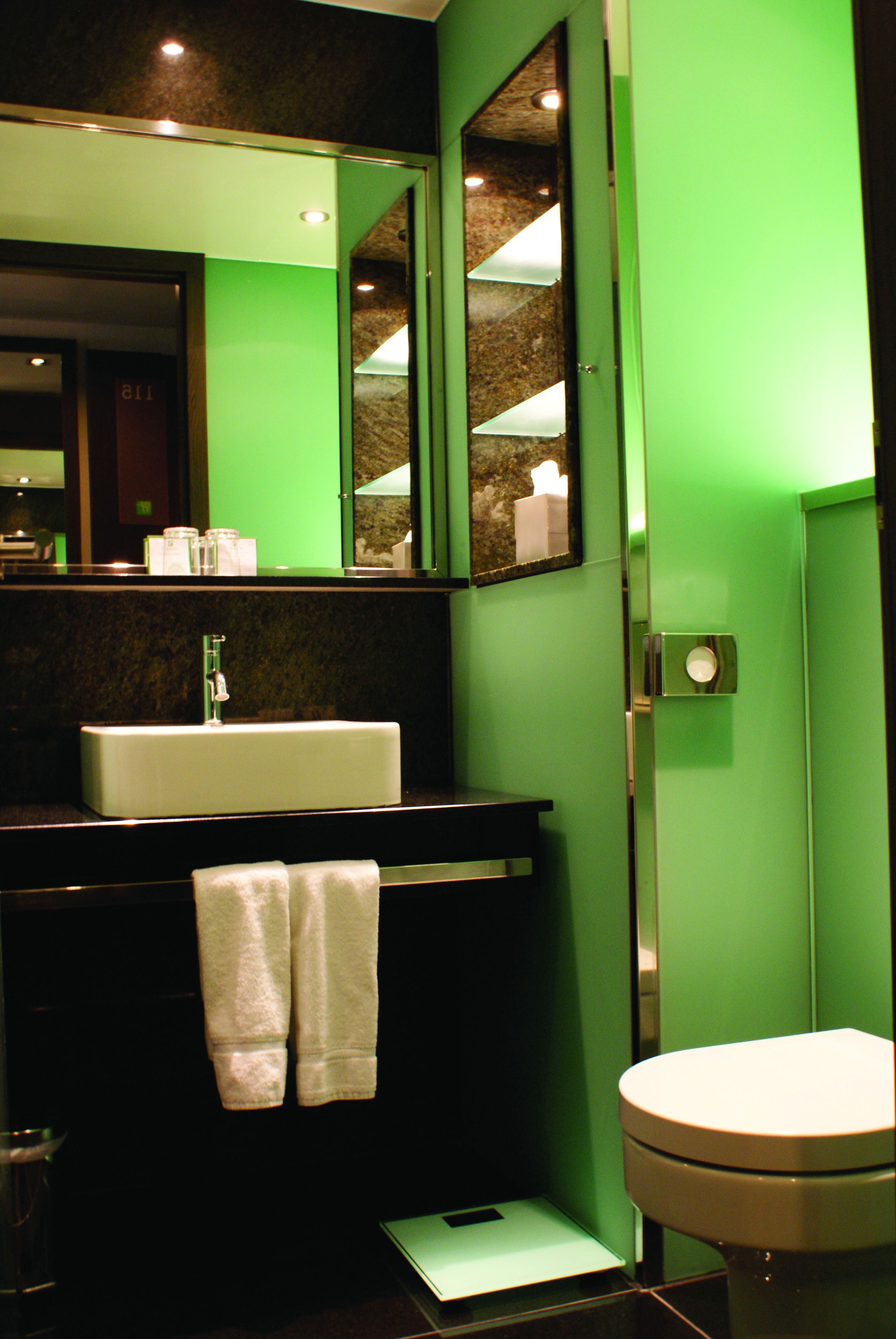 A bathroom with a green wall, a white sink, a mirror, and a toilet.