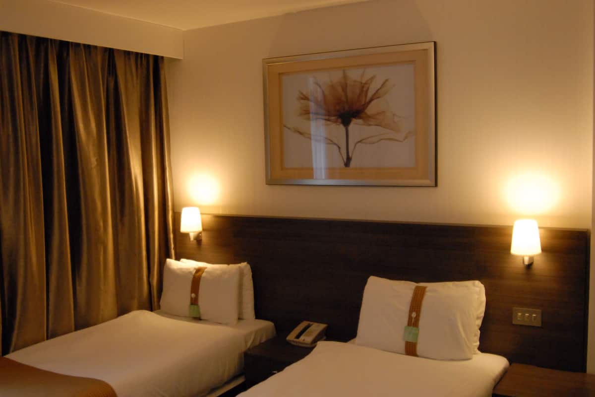 Een hotelkamer met twee bedden, een lijst met een kunstwerk aan de muur en twee bedlampen.