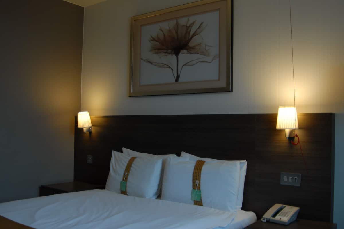Een hotelkamer met een opgemaakt bed, twee bedlampen, een kunstwerk in een lijst aan de muur en een telefoon naast het bed.