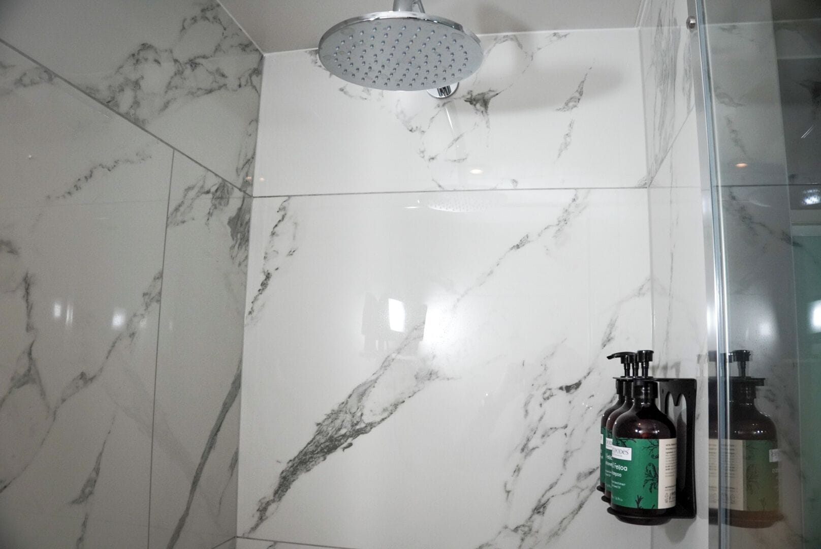A bathroom with a shower, marble tiles, and a bottle of shampoo.
