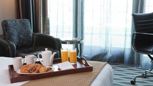 Hotellihuone, jossa on sänky, aamiaistarvikkeilla katettu ruokapöytä, tuoli ja näkymä ulos.