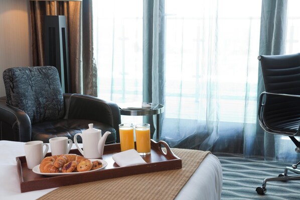 Ein Hotelzimmer mit Bett, einem Esstisch mit Frühstücksangebot, einem Stuhl und Blick ins Freie.