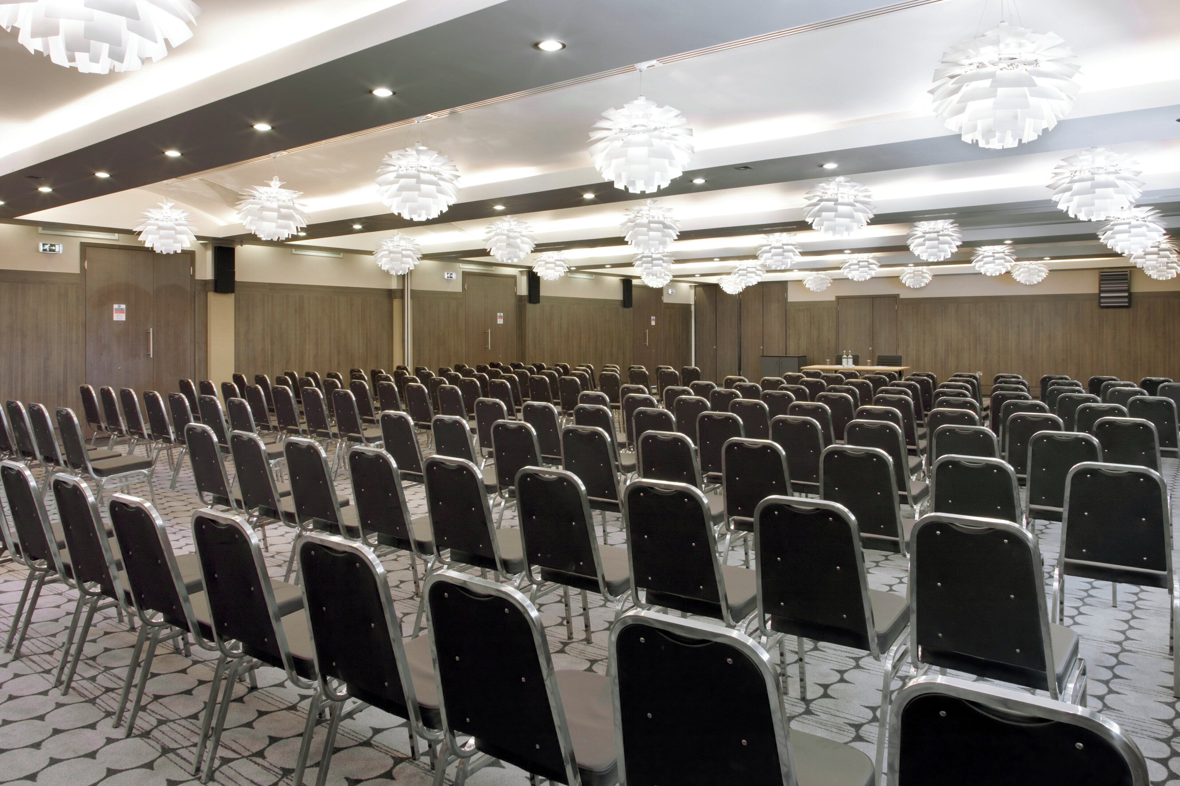 A conference room with rows of chairs, a podium, and modern ceiling lights.