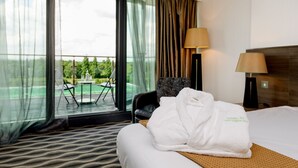 A hotel room with a bed, a chair, a table, and a view of a pool and greenery.