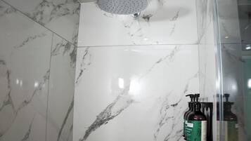 Une salle de bain avec une douche, des carreaux de marbre et deux bouteilles de shampoing posées sur une étagère.