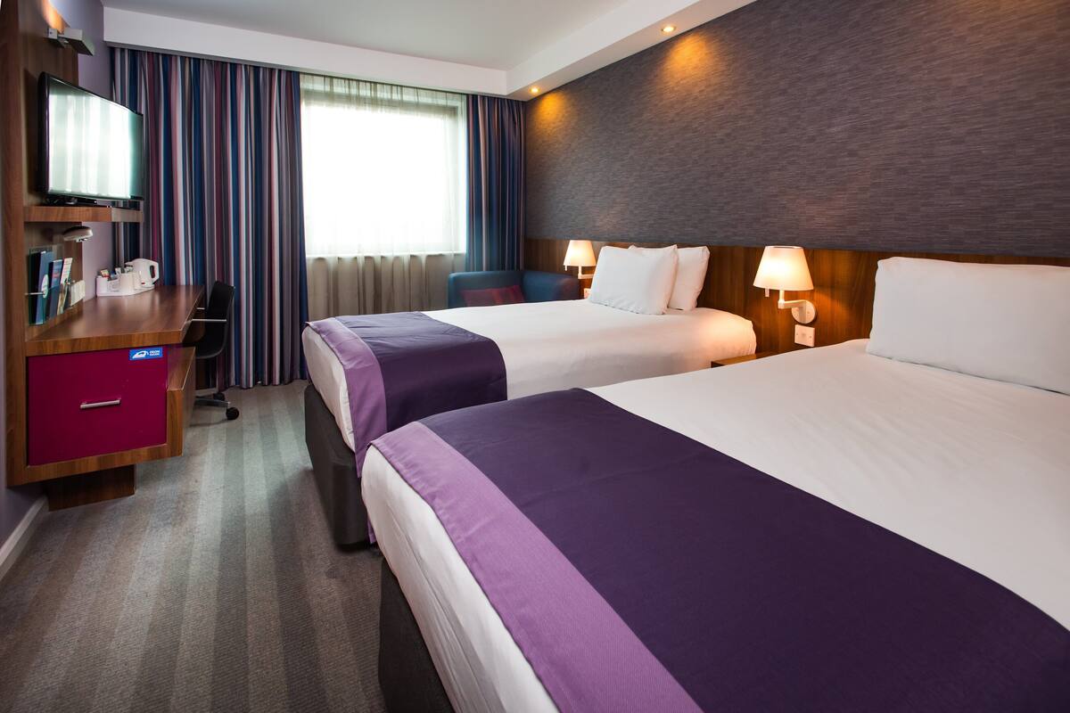 A hotel room with two beds, a desk with a television, a chair, and a desk lamp.