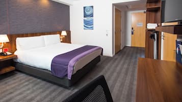 Habitación de hotel con cama, lámparas de noche, escritorio, silla, televisión y puerta al baño.