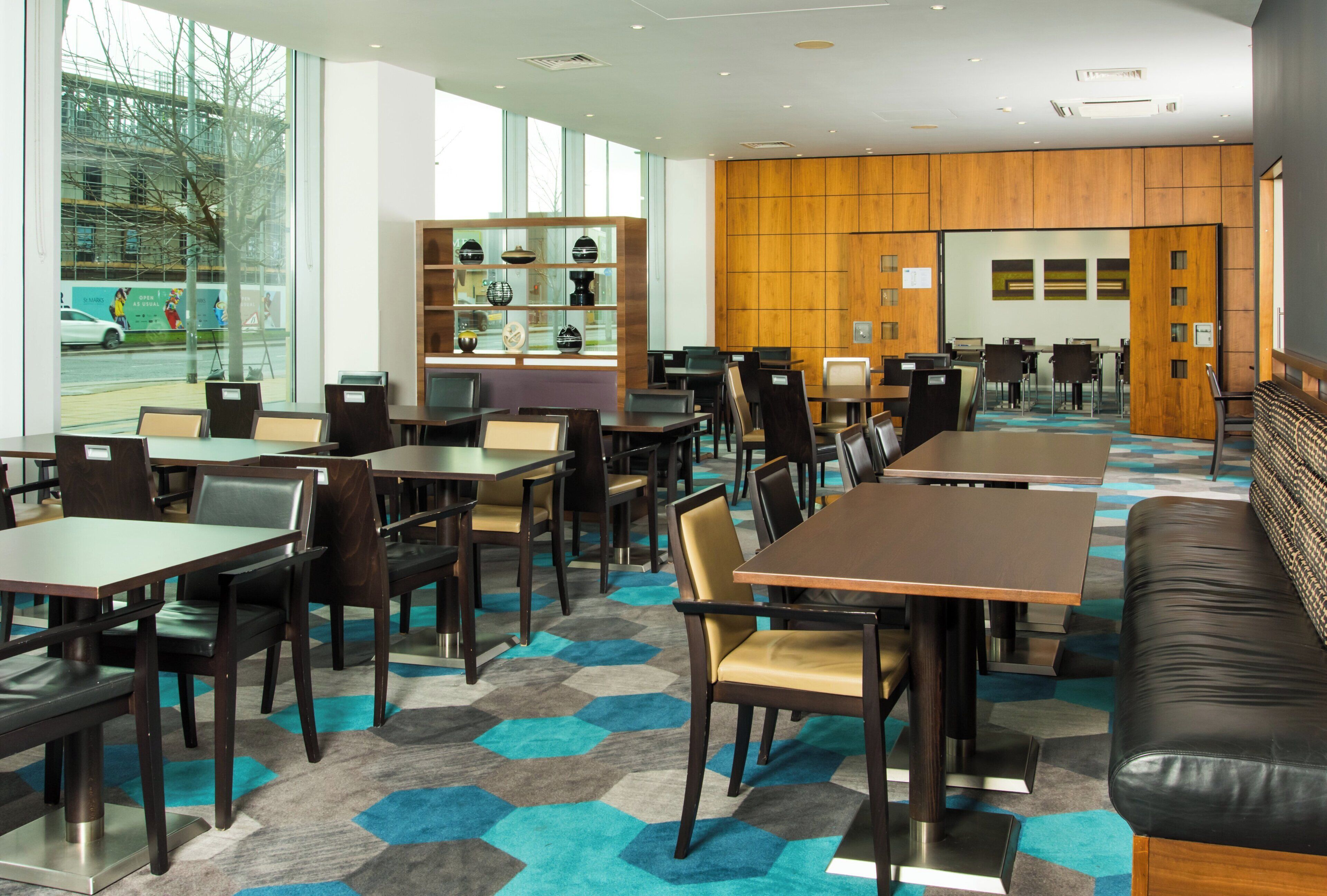 Een moderne eetruimte met meerdere tafels en stoelen, een presentatie van decoratieve objecten, en een uitzicht op de straat door grote ramen.