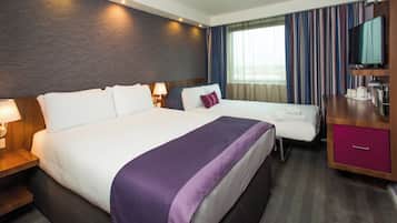 Habitación de hotel con una cama grande, otra más pequeña, un escritorio con televisor y una ventana con cortinas.