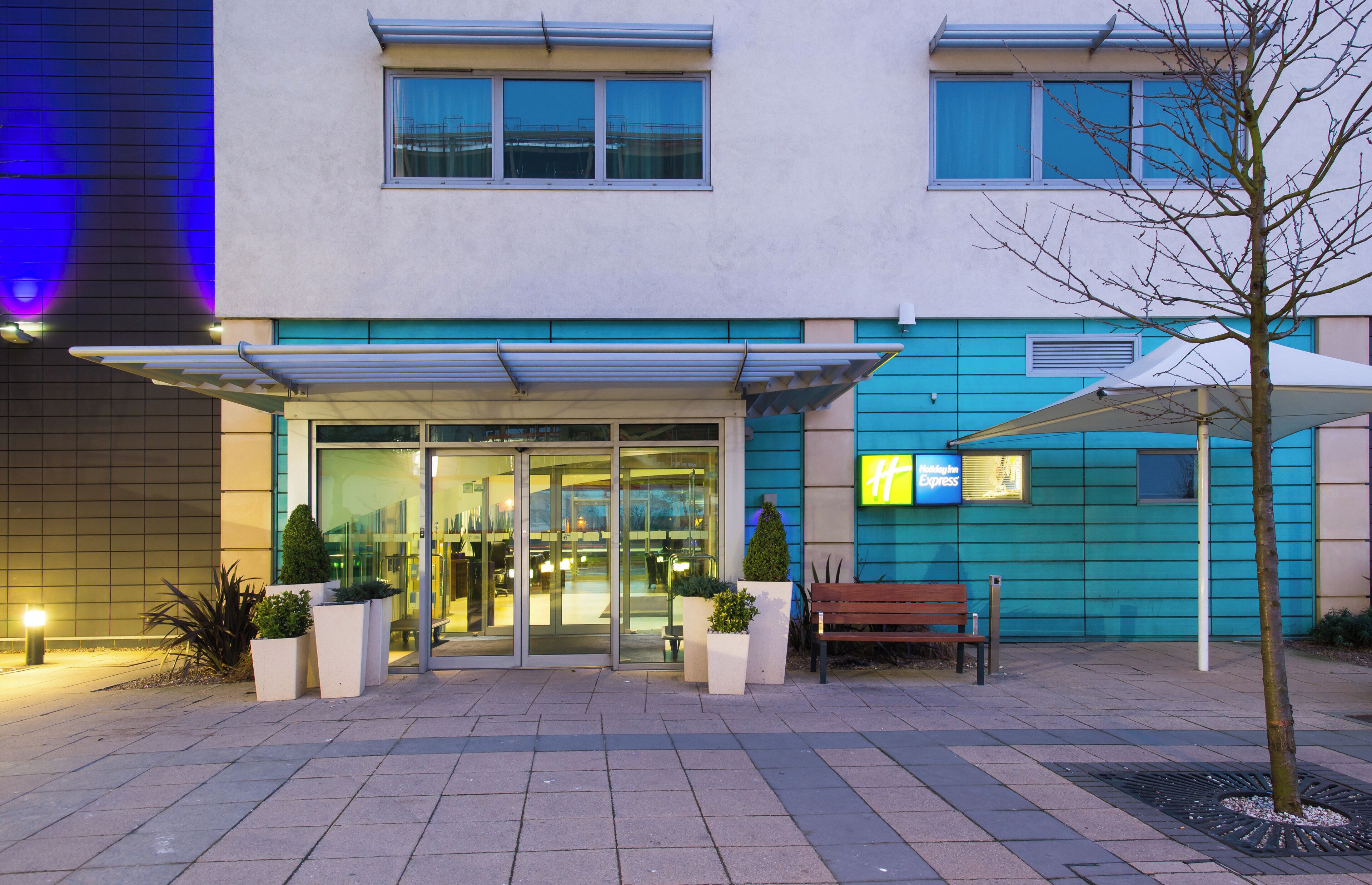 A hotel entrance with a glass door, a bench, and a tree in the foreground.