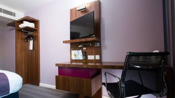 A hotel room with a wooden desk, a television, a chair, and a wardrobe.