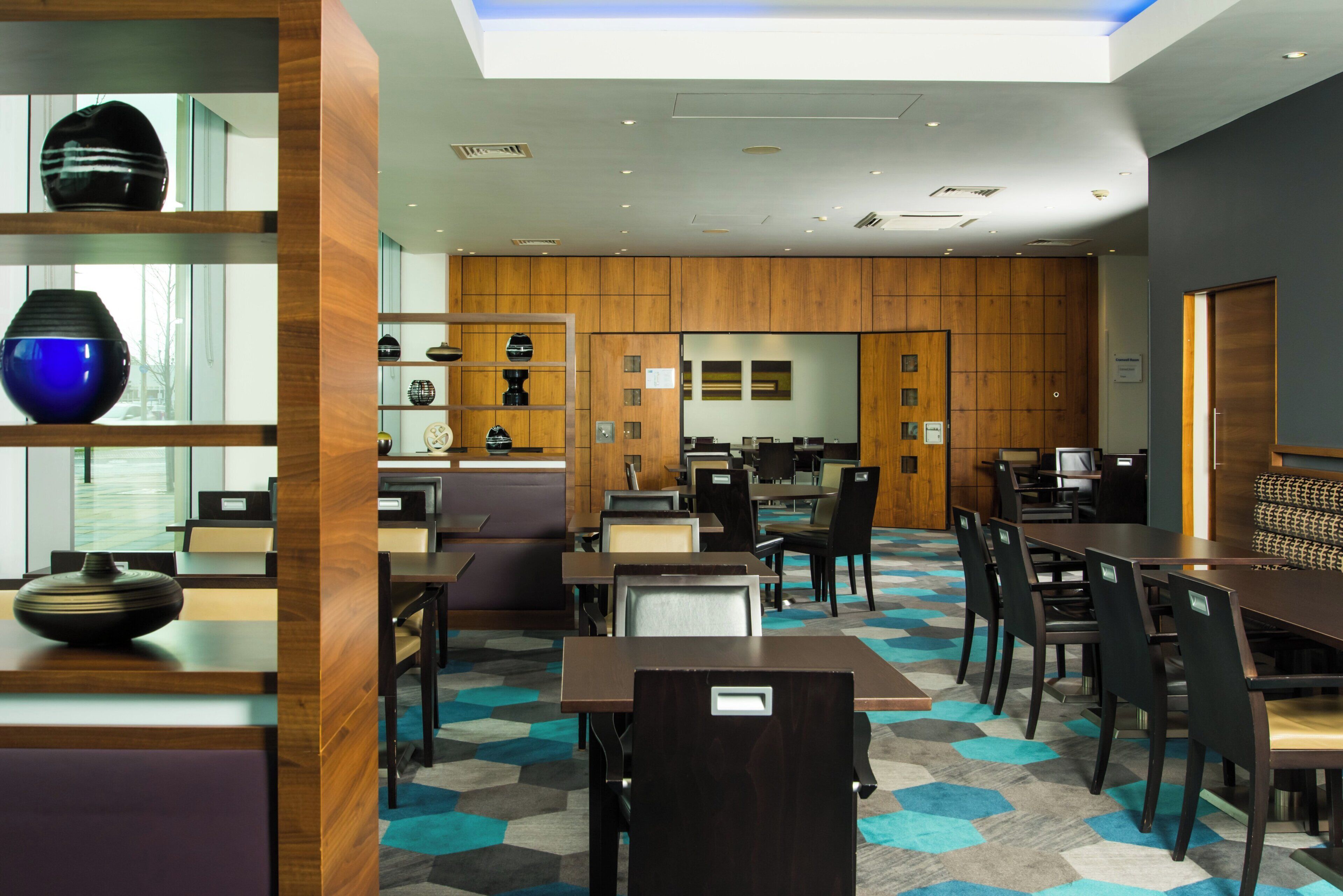 Un hall d’hôtel moderne doté d’un espace salon central, d’un comptoir d’accueil et de divers objets décoratifs disposés sur des étagères.