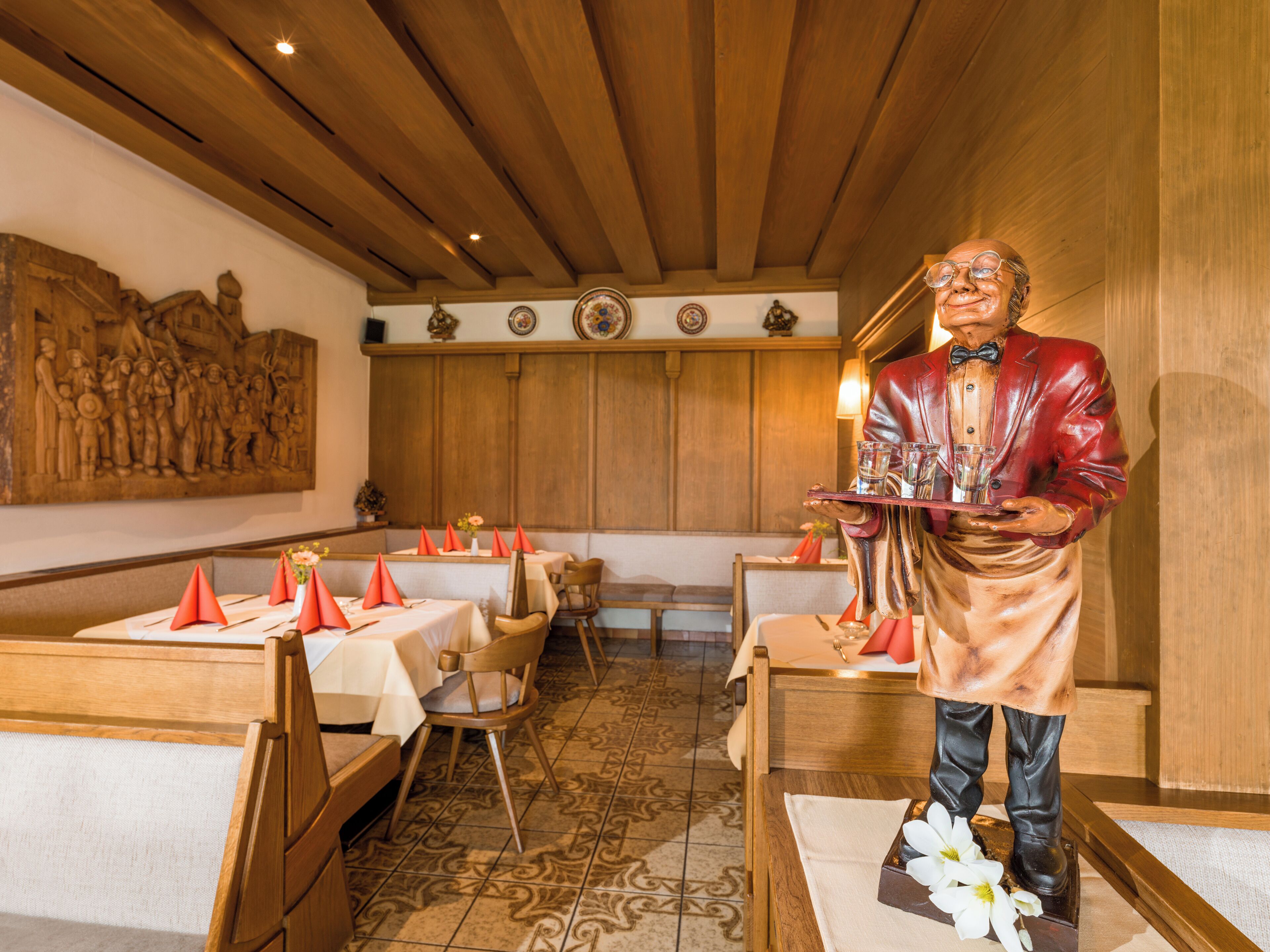 A restaurant with wooden paneling, a mural, and a waiter statue.