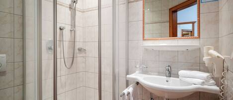 A bathroom with a glass-enclosed shower, a sink with a mirror above it, and a towel rack.