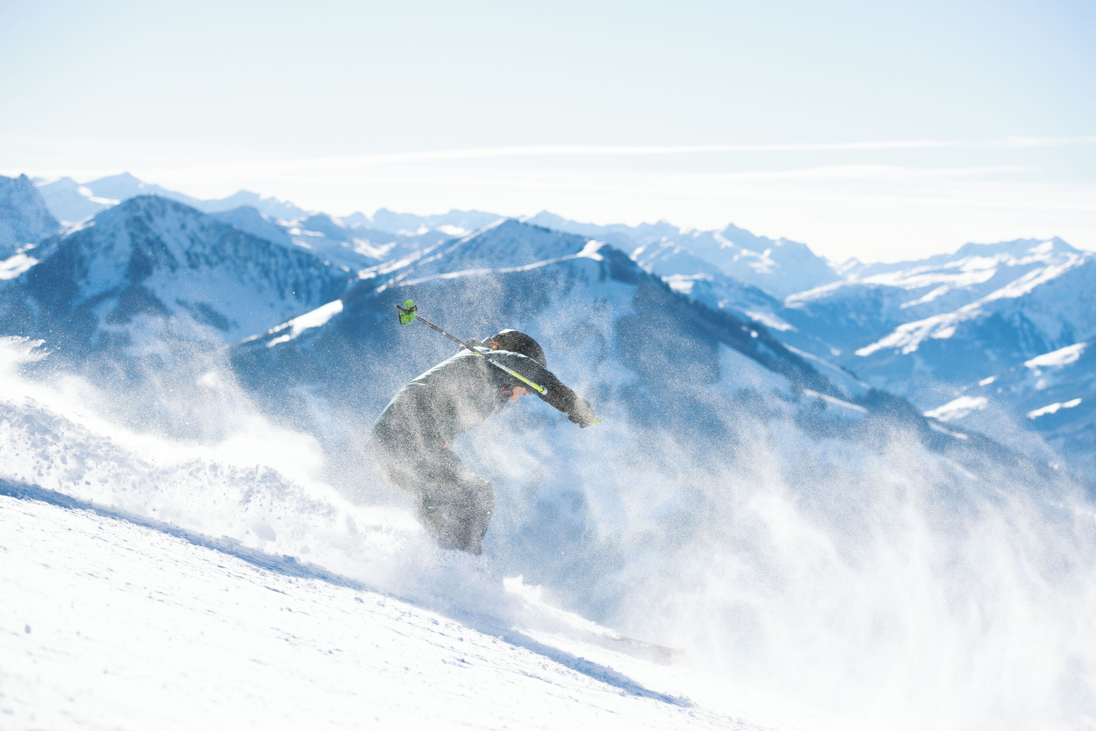 A skier on a snowy mountain slope with snow being kicked up behind them.