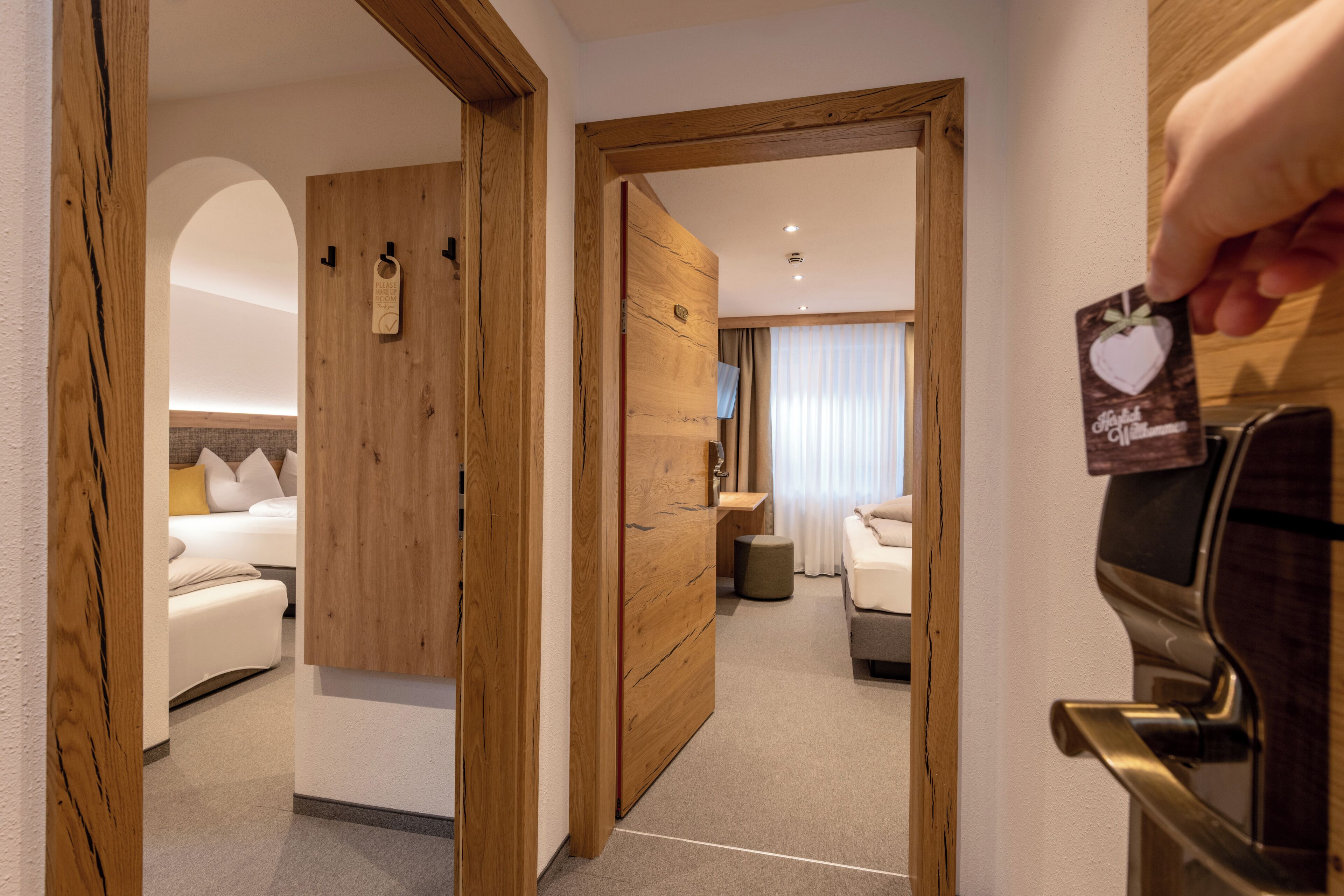 Ein Hotelzimmer mit Holztür, einem Bett mit weißer Bettwäsche, einem kleinen Nachttisch und einem Fernseher.