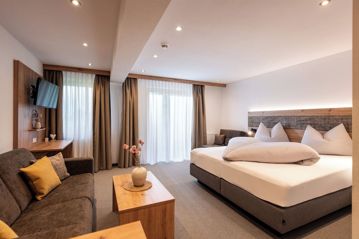 A modern hotel room with a large bed, a sofa, a TV, and a desk.