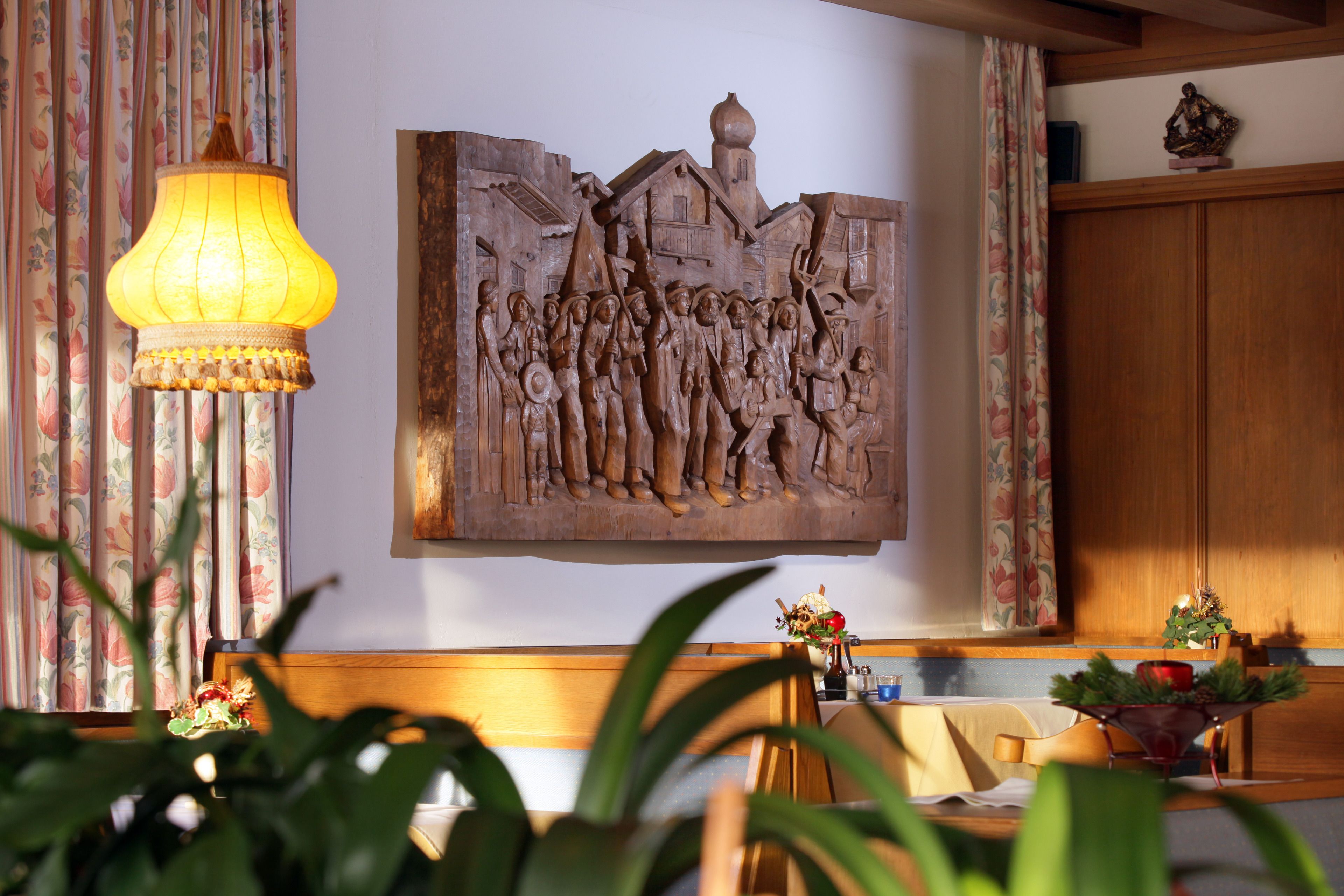 A dining area with a wooden table, chairs, a lamp, and a wall-mounted sculpture.