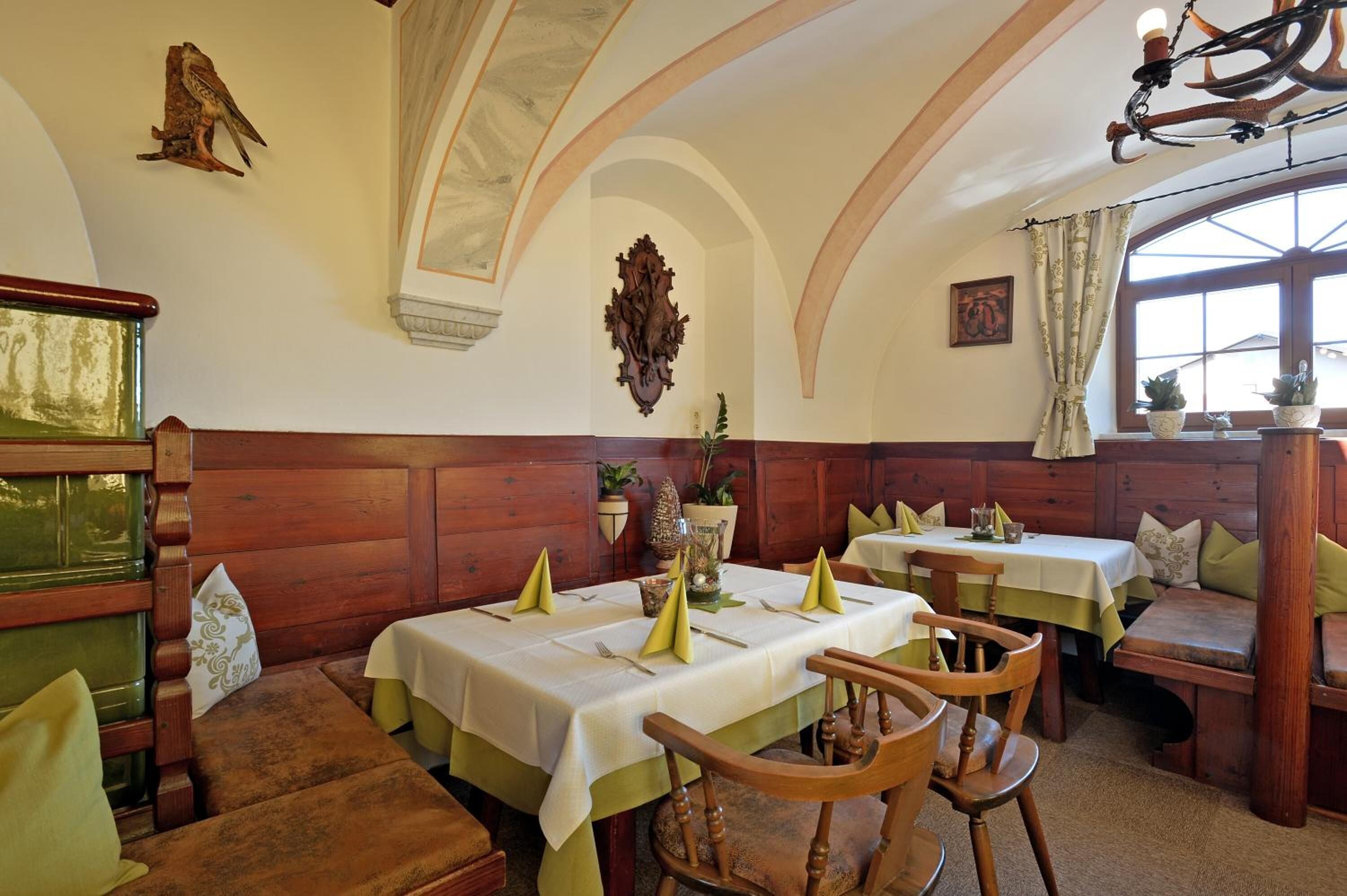 A dining area with wooden benches and tables, a chandelier, and a decorative wall piece.