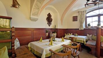 A dining area with wooden benches and tables, a chandelier, and a decorative wall piece.