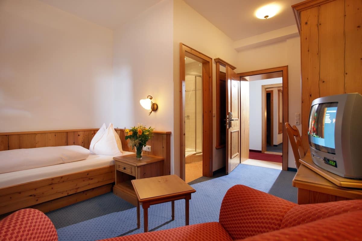 A hotel room with a bed, a small table with a vase of flowers, a television, and a wooden cabinet.