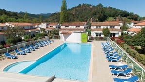Une piscine entourée de chaises longues, elle-même bordée de bâtiments aux toits recouverts de tuiles rouges, le tout se dressant sur un fond de collines.