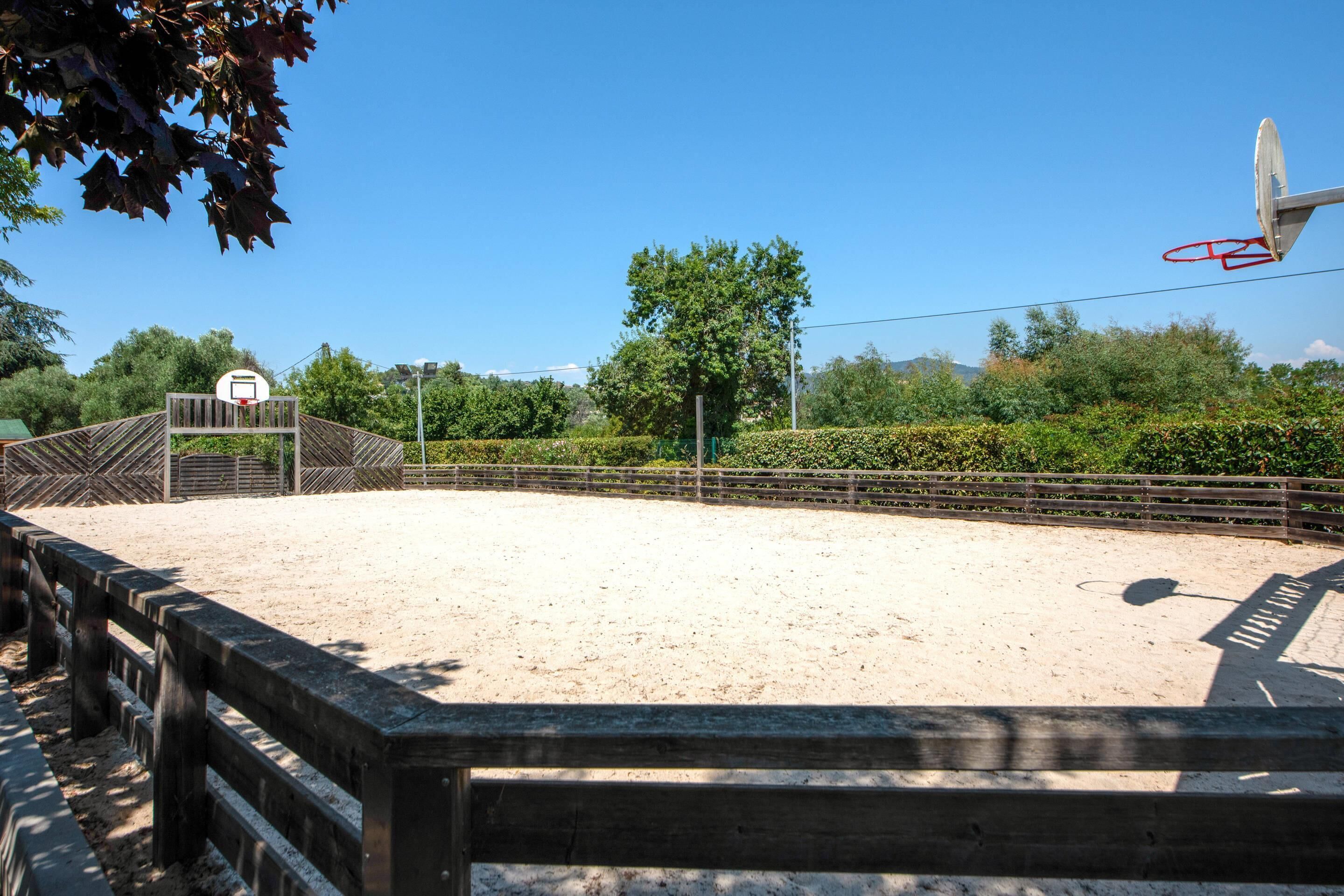 An outdoor basketball court with a wooden fence, a basketball hoop, and a clear blue sky.