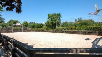 An outdoor basketball court with a wooden fence, a basketball hoop, and a clear blue sky.