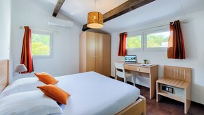 Une chambre d’hôtel avec un lit, un bureau, une chaise et un petit meuble en bois.