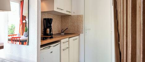 A compact kitchen with white cabinets, a coffee maker, and a sink.