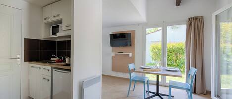 Uma cozinha moderna com armários brancos, micro-ondas embutido e máquina de lavar louça. Há uma área de refeições com mesa e cadeiras, e uma TV fixada na parede.