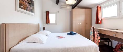 A bedroom with a wooden bed, a desk, and a window with curtains.