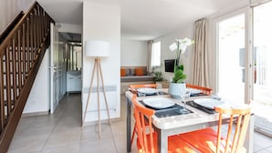 Un coin repas avec une table dressée pour quatre personnes, une lampe et un escalier menant à une autre pièce.