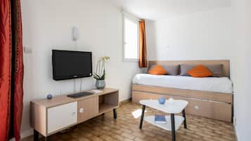 Une chambre d’hôtel de taille réduite, comprenant un lit, une télévision, une petite table et un bureau agrémenté d’une plante.