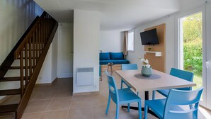 Un salon moderne avec un escalier en bois, un coin repas avec des chaises bleues, un canapé et un téléviseur fixé au mur.