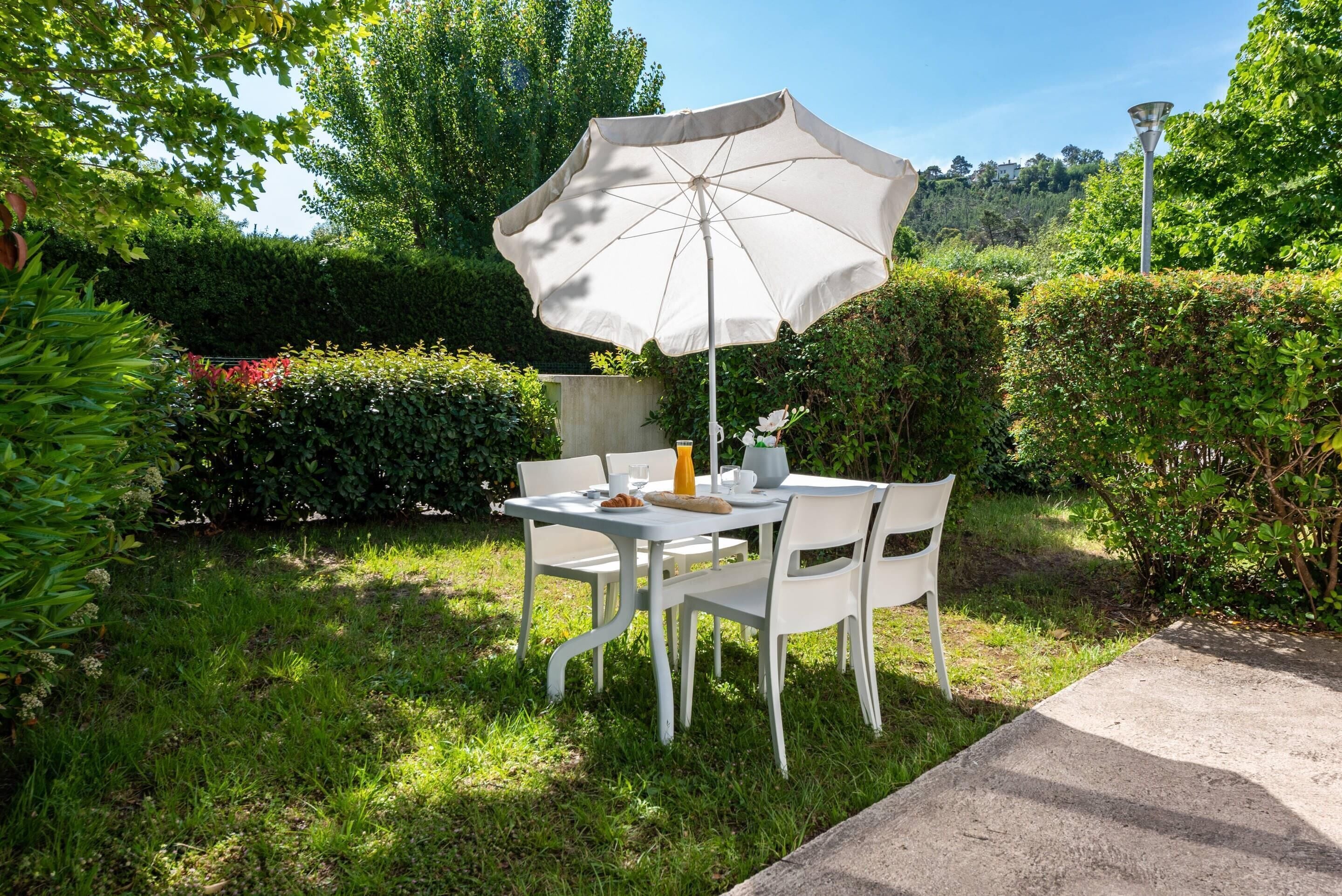 An outdoor dining area with a table and chairs, an umbrella, and a lamp post.
