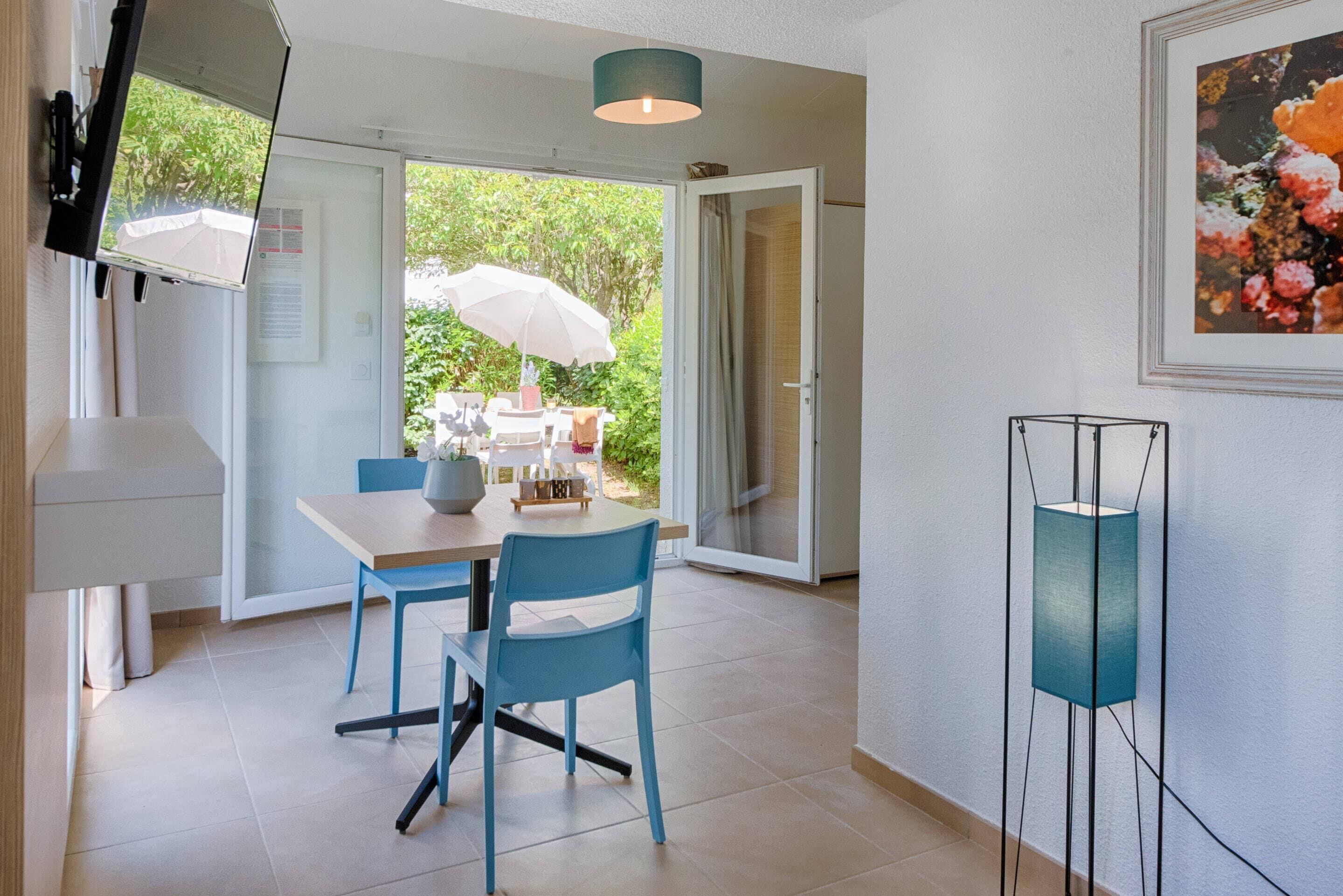 Uma área de jantar moderna com mesa e cadeiras, uma luminária no teto e vista para o verde lá fora.