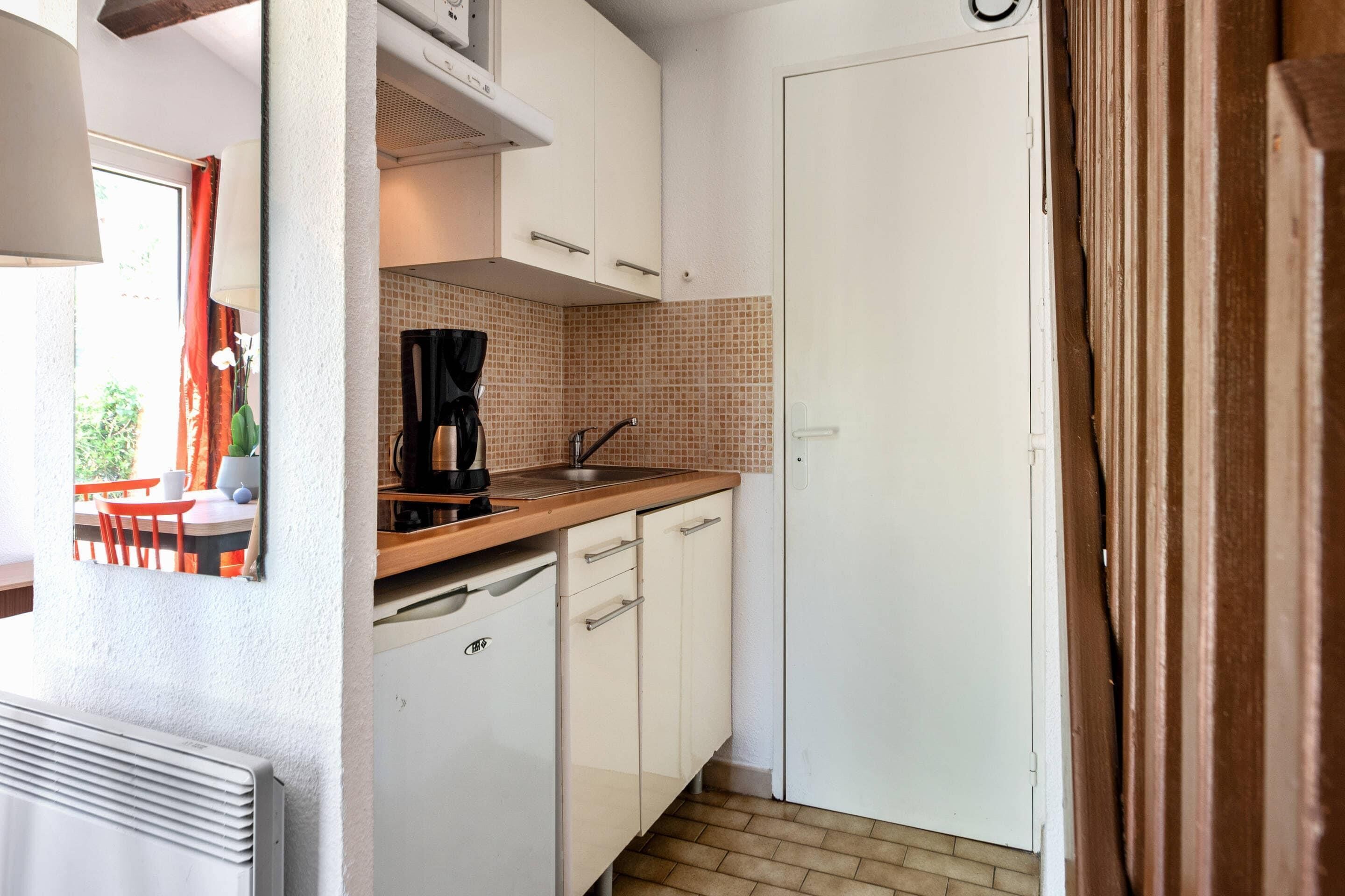 A compact kitchen with white cabinets, a coffee maker, and a tiled backsplash.