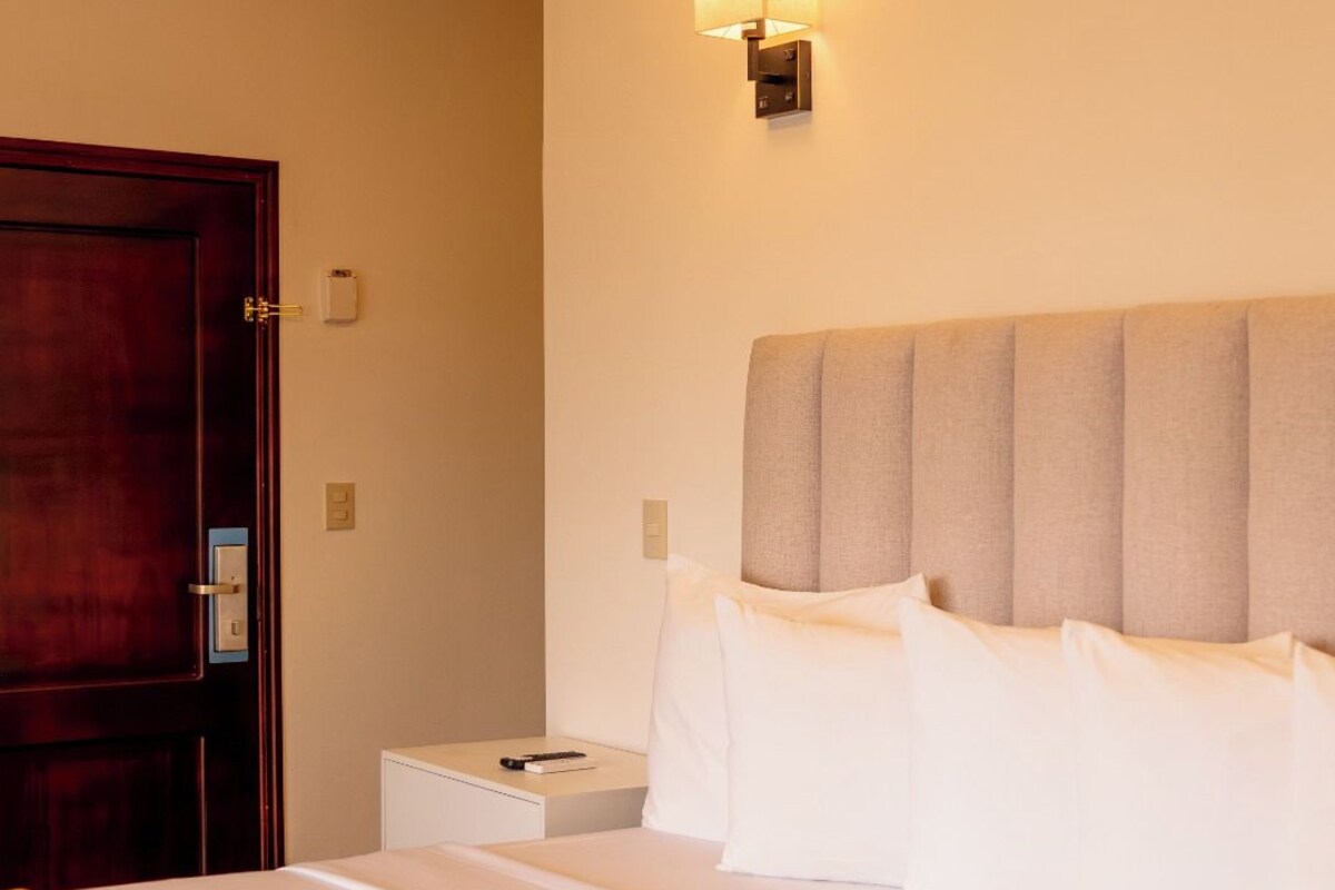 Una habitación de hotel con una cama, una mesita de noche, una lámpara de pared y una puerta.