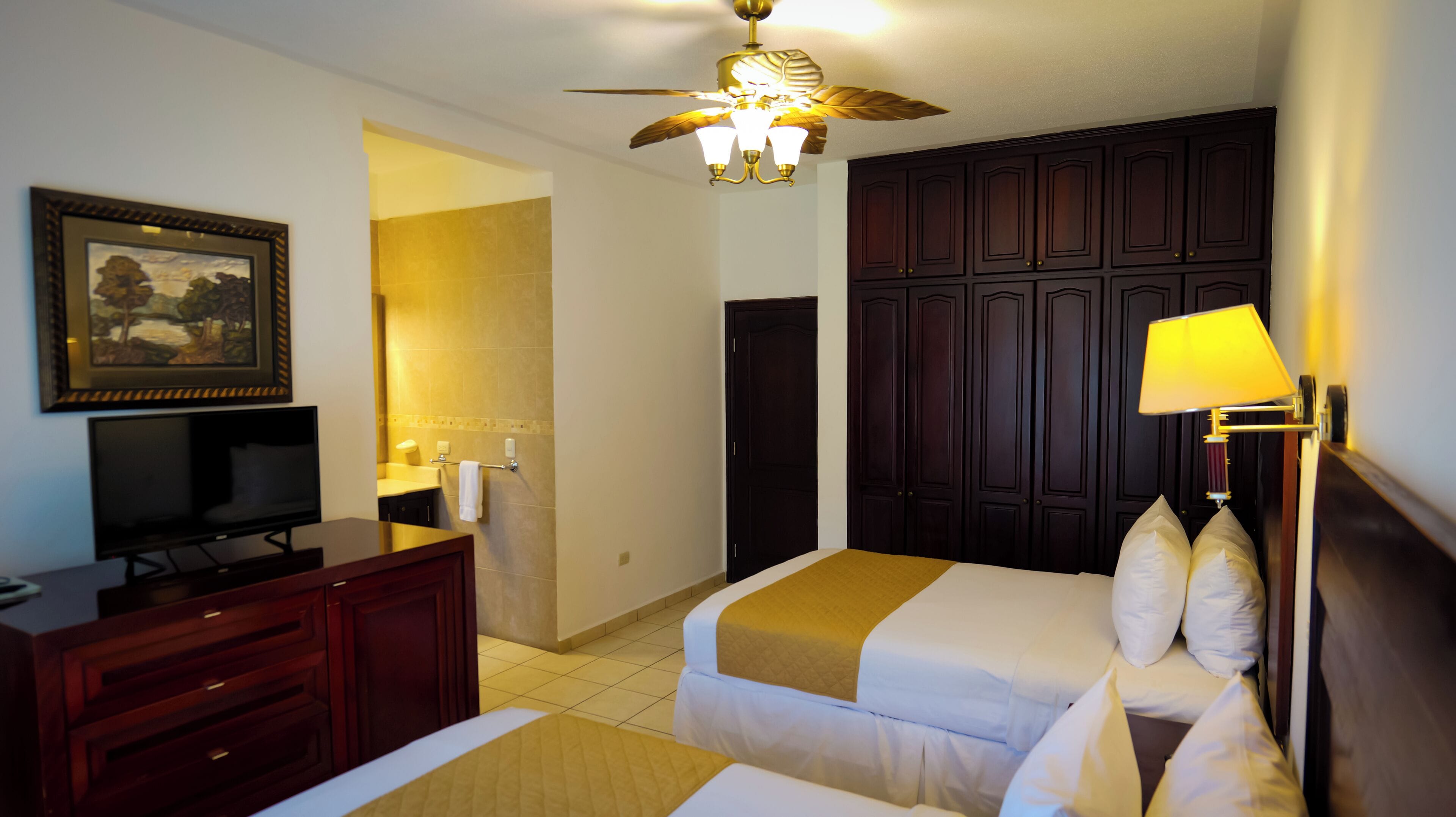 A hotel room with a bed, a desk, a TV, a ceiling fan, and a wardrobe.
